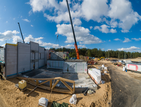 Aerial view of a construction site with a mobile crane lifting concrete panels workers on site and a forest background in Latvia. Aerial view of a construction site with a mobile crane lifting concrete panels workers on site and a forest background in Latvia.