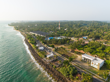 Aerial view of the coastline featuring a rocky breakwater a coastal road and lush tropical vegetation in Galle Southern Province Sri Lanka.