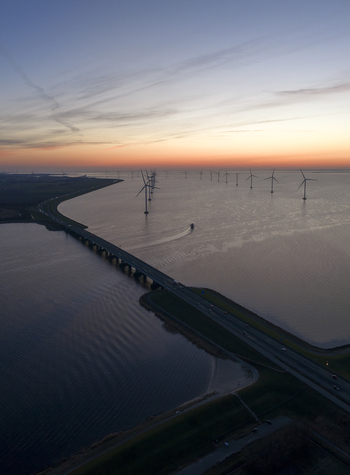 Aerial view of the Ketelbrug bridge spanning across the water with offshore wind turbines and a boat at sunset in Nagele Flevoland Netherlands.