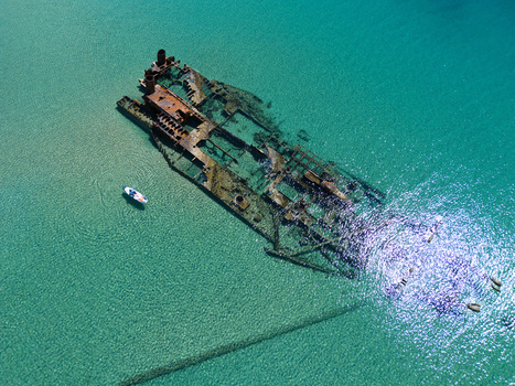 Aerial view of the rusty Shipwreck Epanomi submerged in turquoise crystal clear water with a small boat nearby in Epanomi Greece.