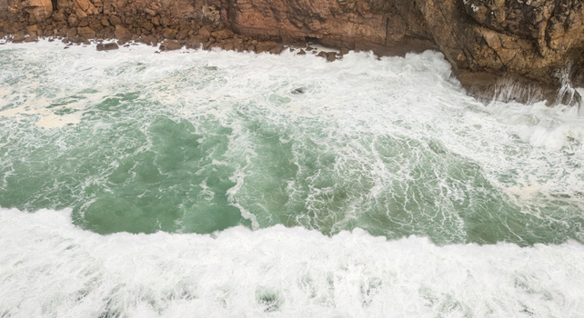Aerial view of powerful turquoise waves crashing against the rugged rocky cliffs of Sagres Faro Portugal. Aerial view of powerful turquoise waves crashing against the rugged rocky cliffs of Sagres Faro Portugal.