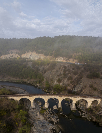 Aerial view of a historic stone railway bridge spanning a river in a misty forested valley near Balabanovo Kardzhali Province Bulgaria. Aerial view of a historic stone railway bridge spanning a river in a misty forested valley near Balabanovo Kardzhali Province Bulgaria.