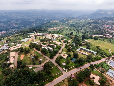 Aerial view of a sprawling campus with multiple buildings paved roads and lush green hills under an overcast sky in Ghana. Aerial view of a sprawling campus with multiple buildings paved roads and lush green hills under an overcast sky in Ghana.