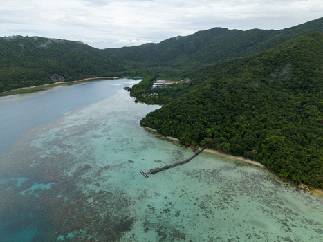 Aerial view of a wooden pier stretching into the turquoise waters meeting lush green hills under a cloudy sky at Turtle Conservation Karimunjawa Central Java Indonesia.