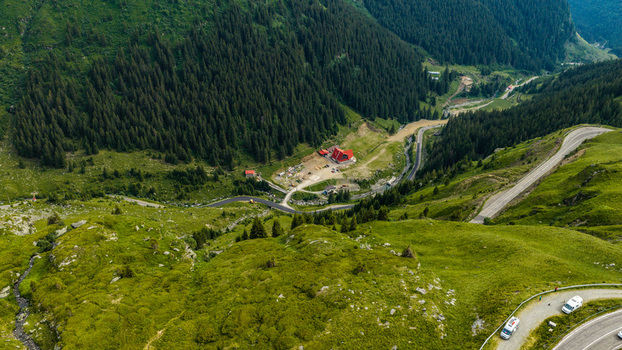 Aerial view of the Transfagarasan mountain road winding through lush green valleys and dense pine forests in Curtea de Arges Judetul Arges Romania.