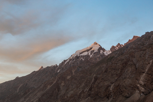 View of the snow capped peaks of the Baltoro Glacier under a soft sunset sky with rugged rocky slopes in Baltoro Gilgit Baltistan Pakistan.
