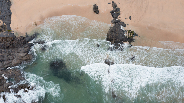 Aerial view of Harlyn Bay Beach with waves crashing against dark rocks and golden sand in Saint Merryn Cornwall United Kingdom.