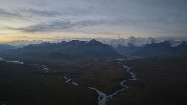 Aerial view of Engilchek Glacier with winding rivers flowing through the vast mountain valley under a soft sunset sky in Ak Su Issyk Kul Region Kyrgyzstan. Aerial view of Engilchek Glacier with winding rivers flowing through the vast mountain valley under a soft sunset sky in Ak Su Issyk Kul Region Kyrgyzstan.
