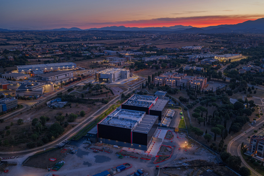 Aerial view of a modern datacenter complex at sunset featuring large industrial buildings surrounding roads and trees in Settecamini Lazio Italy.