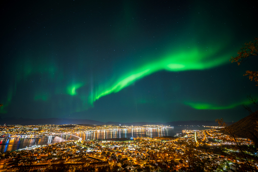 View of the aurora borealis illuminating the night sky above the city lights and waterfront of Tromso Troms Norway. View of the aurora borealis illuminating the night sky above the city lights and waterfront of Tromso Troms Norway.