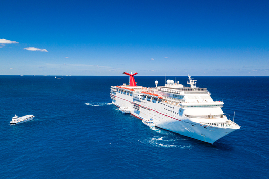 The Berry Islands The Bahamas 02 May 2020 Aerial view of a large cruise ship sailing in the deep blue waters of the Atlantic Ocean with small support vessels nearby under a clear sky.