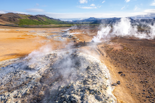 Aerial view of Hverir geothermal field with steaming fumaroles bubbling mud pots and vibrant orange hued volcanic soil under a clear blue sky in Reykjahlid Thingeyjarsveit Iceland.