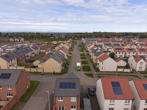 Aerial view of modern residential houses with solar panels on rooftops and a green truck on a suburban street in Edinburgh Scotland United Kingdom.