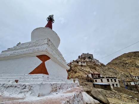 View of the white stupa at Chemrey Gompa with monastery buildings perched on the rocky hillside in Chemrey Ladakh India.