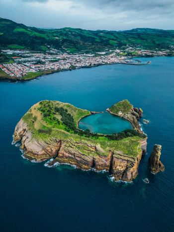 Aerial view of a stunning islet with a crater lake vibrant green vegetation and rugged cliffs surrounded by the deep blue sea Vila Franca do Campo Portugal.