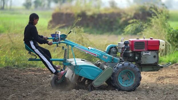 View of a young woman operating a power tiller in a field Nepal. View of a young woman operating a power tiller in a field Nepal.