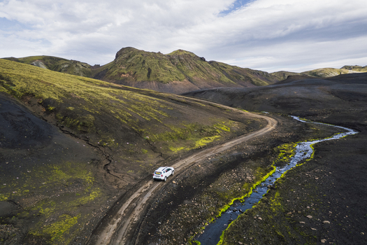 Aerial view of a white SUV driving on the winding F235 dirt road through volcanic hills and mossy landscapes in Highlands of Iceland Iceland. Aerial view of a white SUV driving on the winding F235 dirt road through volcanic hills and mossy landscapes in Highlands of Iceland Iceland.