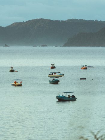 View of small boats floating on the calm sea with distant hills under a cloudy sky in Costa Rica.