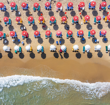 Aerial view of Bat Yam beach with rows of red and white umbrellas on the sand and waves crashing on the shore in Bat Yam Center District Israel. Aerial view of Bat Yam beach with rows of red and white umbrellas on the sand and waves crashing on the shore in Bat Yam Center District Israel.