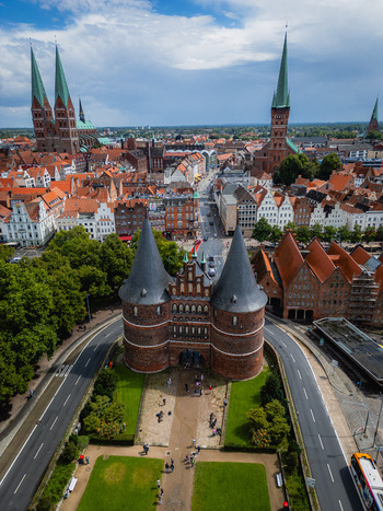 Aerial view of the iconic Holstentor gate stands guard over the city its red brick contrasting with the green spaces and distant church spires L&uuml;beck Schleswig Holstein Germany.