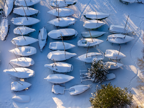 Aerial view of rows of sailboats covered in thick white snow with long shadows on a sunny winter day in Trakai Vilnius County Lithuania. Aerial view of rows of sailboats covered in thick white snow with long shadows on a sunny winter day in Trakai Vilnius County Lithuania.