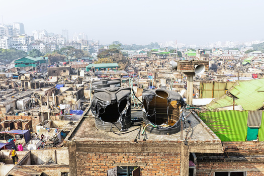 Aerial view of Korail Basti showing dense housing damaged rooftops and large water tanks on a brick structure with the city skyline in the background. Dhaka Dhaka Division Bangladesh.