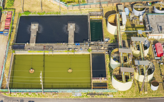 Aerial view of a wastewater treatment plant featuring large rectangular settling tanks with green and dark water circular storage tanks and industrial infrastructure in Taiwan. Aerial view of a wastewater treatment plant featuring large rectangular settling tanks with green and dark water circular storage tanks and industrial infrastructure in Taiwan.