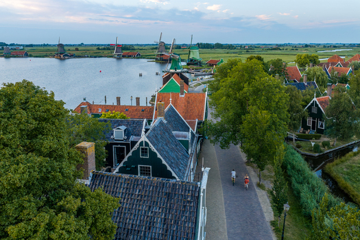 Zaandam Netherlands 26 July 2026 Aerial view of Zaanse Schans windmills along the river with traditional green houses and people cycling on a path during golden hour.