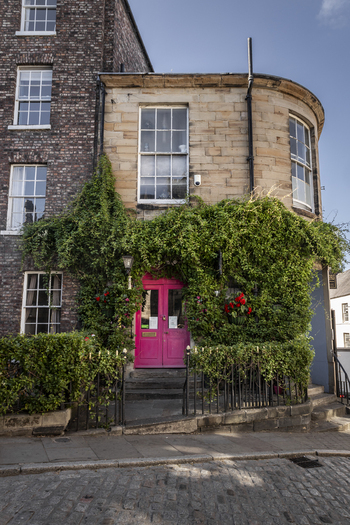 View of a historic building with a vibrant pink door and lush green ivy climbing the stone facade on a cobblestone street in Durham England United Kingdom. View of a historic building with a vibrant pink door and lush green ivy climbing the stone facade on a cobblestone street in Durham England United Kingdom.