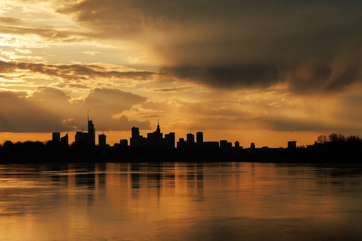 View of the Warsaw city skyline silhouetted against a dramatic golden sunset with reflections on the Vistula River Warsaw Masovian Voivodeship Poland.