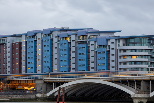 View of modern apartment buildings with blue and grey facades situated behind a bridge with a passing train in London England United Kingdom. View of modern apartment buildings with blue and grey facades situated behind a bridge with a passing train in London England United Kingdom.
