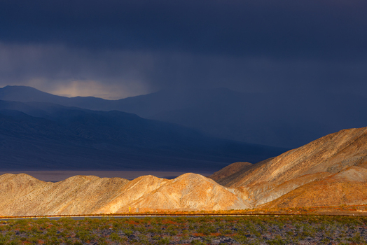 View of Death Valley National Park with golden lit desert hills under a dramatic dark stormy sky in the United States.
