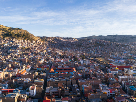Aerial view of the city of Puno nestled in the Andes mountains featuring dense urban housing terracotta rooftops and the surrounding hilly landscape under a clear sky in Puno Puno Peru.