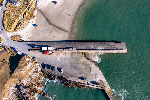 Aerial view of Portnablagh pier and harbour with a small boat parked cars and sandy beach along the rugged coastline in Portnablagh County Donegal Ireland. Aerial view of Portnablagh pier and harbour with a small boat parked cars and sandy beach along the rugged coastline in Portnablagh County Donegal Ireland.