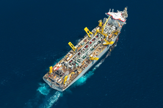 Aerial view of a large dredger vessel with yellow cranes navigating through deep blue ocean waters leaving a white wake Vashafaru Haa Alif Atoll Maldives. Aerial view of a large dredger vessel with yellow cranes navigating through deep blue ocean waters leaving a white wake Vashafaru Haa Alif Atoll Maldives.