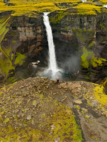 Aerial view of Haifoss waterfall plunging into a deep canyon surrounded by vibrant green mossy cliffs and rocky terrain with a hiker standing on the edge Skeida og Gnupverjah Iceland. Aerial view of Haifoss waterfall plunging into a deep canyon surrounded by vibrant green mossy cliffs and rocky terrain with a hiker standing on the edge Skeida og Gnupverjah Iceland.