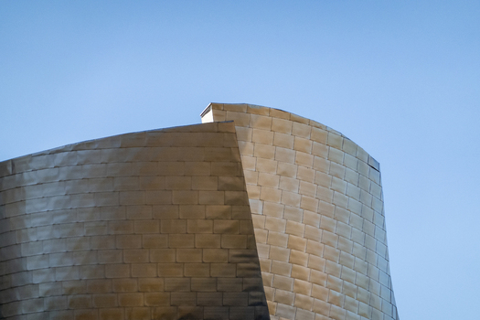 View of the curved titanium panels of the Guggenheim Museum Bilbao reflecting soft light against a clear blue sky Bilbao Euskadi Spain. View of the curved titanium panels of the Guggenheim Museum Bilbao reflecting soft light against a clear blue sky Bilbao Euskadi Spain.