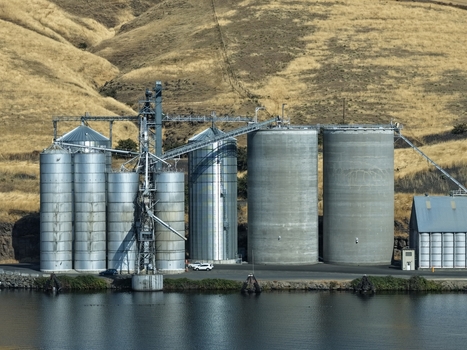 Aerial view of grain silos situated along a riverbank with dry rolling hills in the background in Whitman County Washington United States. Aerial view of grain silos situated along a riverbank with dry rolling hills in the background in Whitman County Washington United States.