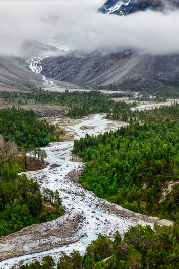 Aerial view of the glacial river flowing through the Faueldalen valley surrounded by lush green forests rocky terrain and misty mountains in Jovik Troms Norway.