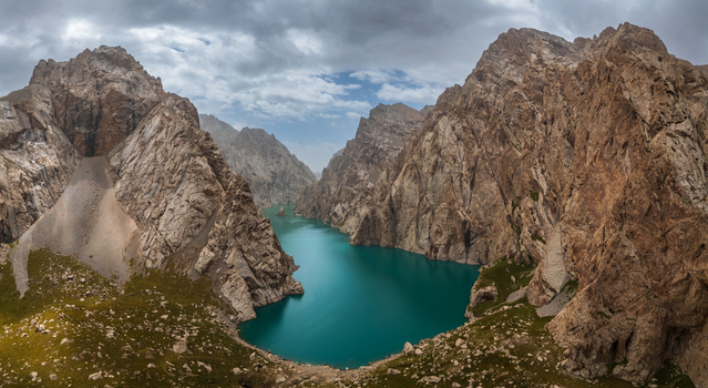 Aerial view of Kol Suu lake nestled between towering rocky cliffs and rugged mountain peaks under a cloudy sky in At Bashi District Naryn Region Kyrgyzstan.