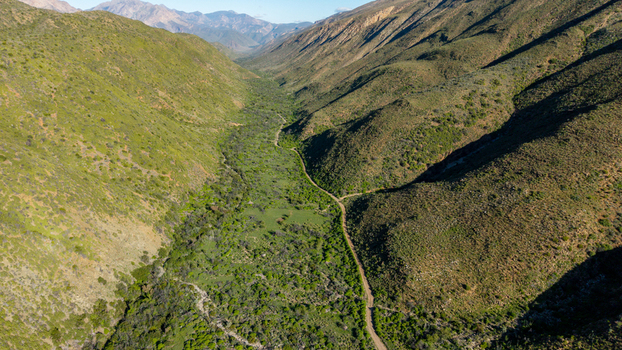 Aerial view of Die Hel Gamkaskloof valley with a winding dirt road surrounded by steep green mountains under a clear sky in Central Karoo District Municipality Western Cape South Africa. Aerial view of Die Hel Gamkaskloof valley with a winding dirt road surrounded by steep green mountains under a clear sky in Central Karoo District Municipality Western Cape South Africa.