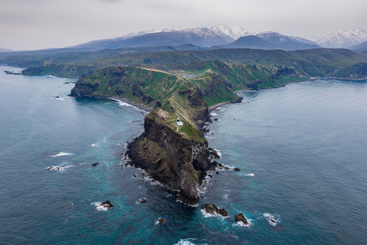 Aerial view of Cape Kamui featuring a lighthouse on a rugged cliff surrounded by the sea with snow capped mountains in the background in Otaru Hokkaido Japan. Aerial view of Cape Kamui featuring a lighthouse on a rugged cliff surrounded by the sea with snow capped mountains in the background in Otaru Hokkaido Japan.