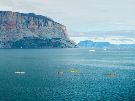 Aerial view of Uummannaq mountain rising above the sea with four colorful kayaks paddling in the water in Uummannaq Kitaa Greenland. Aerial view of Uummannaq mountain rising above the sea with four colorful kayaks paddling in the water in Uummannaq Kitaa Greenland.