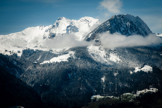 View of majestic snow capped mountains pierce the sky their peaks veiled in ethereal clouds as seen from the train Train from Lucerne to Interlaken Switzerland. View of majestic snow capped mountains pierce the sky their peaks veiled in ethereal clouds as seen from the train Train from Lucerne to Interlaken Switzerland.