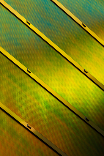 View of a striking architectural facade with diagonal bands of gold against a shimmering iridescent green and bronze surface La Defense Flevoland Netherlands. View of a striking architectural facade with diagonal bands of gold against a shimmering iridescent green and bronze surface La Defense Flevoland Netherlands.