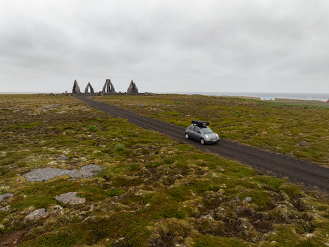 Aerial view of Arctic Henge with its stone structures on a mossy landscape and a car driving on a gravel road under a cloudy sky in Raufarhofn Nordurthing Iceland.