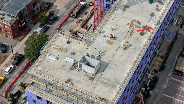 Aerial view of a construction site at Cherry Creek with workers on the concrete rooftop a red crane and building materials in Denver Colorado United States. Aerial view of a construction site at Cherry Creek with workers on the concrete rooftop a red crane and building materials in Denver Colorado United States.
