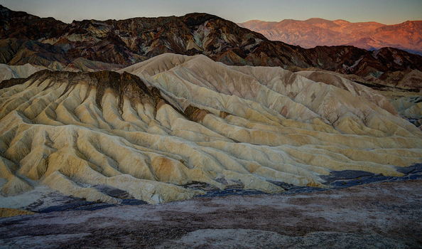 View of the rugged eroded badlands of Zabriskie Point featuring golden hued sediment layers and dramatic shadows under the soft light of dawn in Death Valley California United States.
