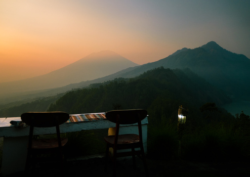 View of two wooden chairs on a terrace overlooking the volcanic landscape of Mount Batur at sunrise with a glowing torch nearby Kintamani Bali Indonesia.