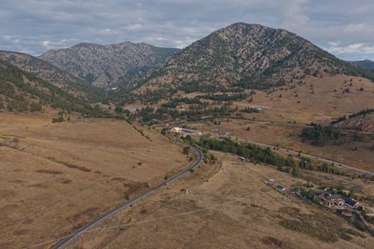 Aerial view of the mountainous landscape near Golden featuring a winding road dry grassy hills pine trees and a small building complex in Golden Colorado United States.